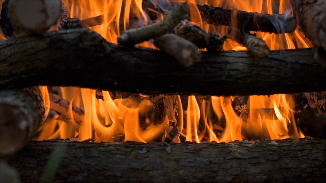 Log cabin fire lay burning with bright orange flames between stacked logs — wilderness survival fire craft