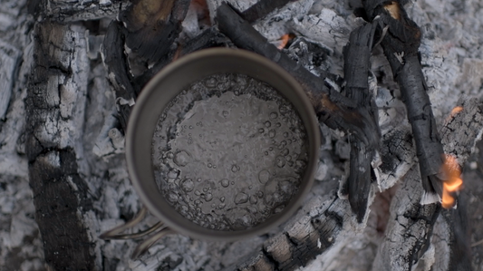 Metal cup boiling water over fire coals — wilderness water disinfection by boiling