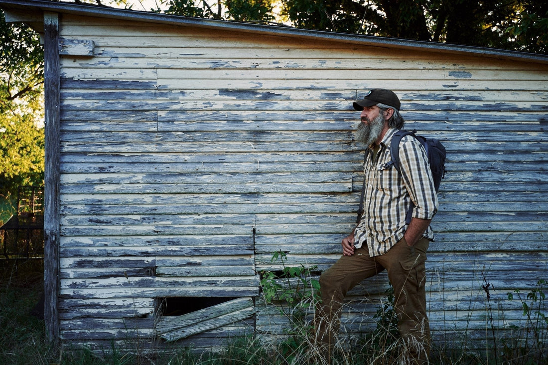 Joshua Enyart walks past a weathered wood-sided shed at sunset, loaded backpack on, ready to move out.