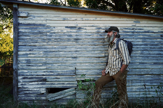 Joshua Enyart walks past a weathered wood-sided shed at sunset, loaded backpack on, ready to move out.