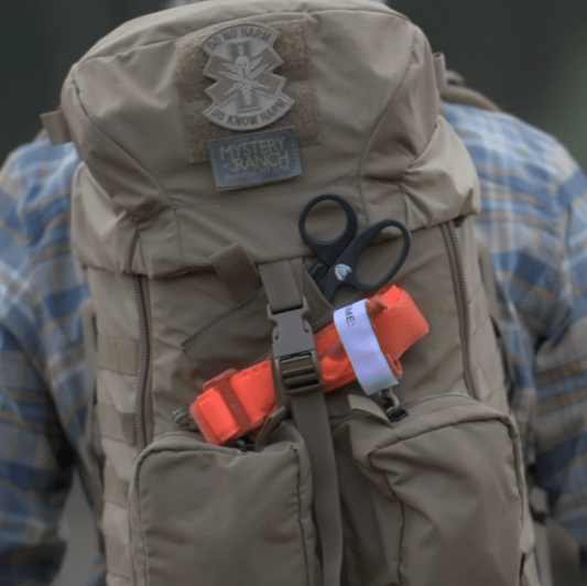 Tactical backpack with trauma shears and tourniquet mounted externally — wilderness field first aid kit