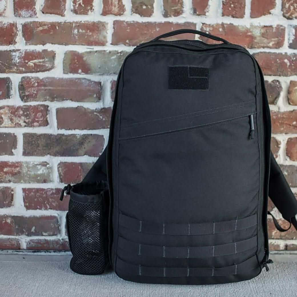 Black GoRuck rucksack with mesh water bottle pocket attached to the side in an urban brick background setting