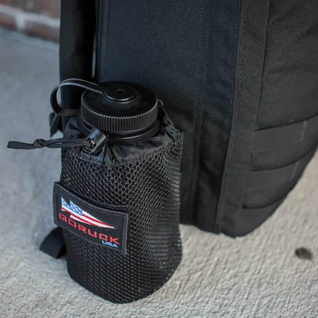 Black GoRuck rucksack with mesh water bottle pocket attached to the side sitting on a concrete floor