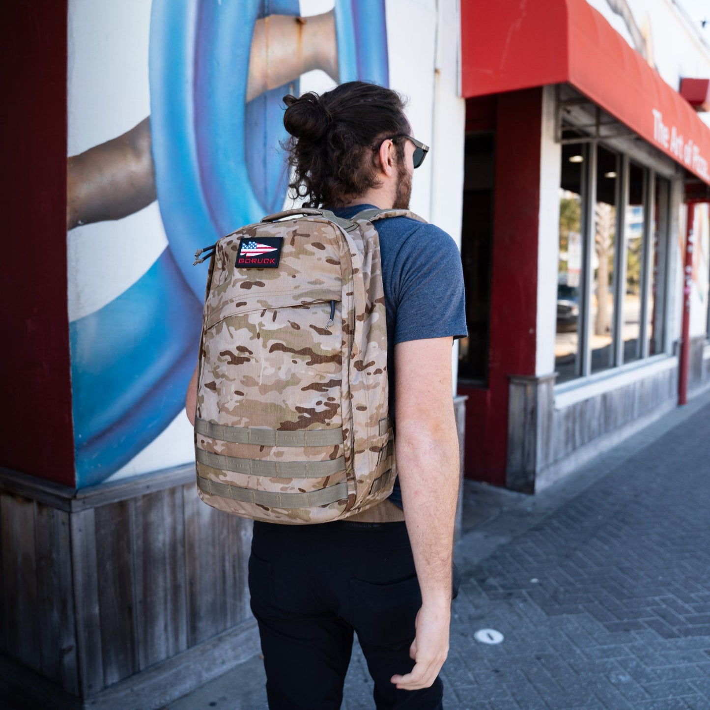 Man in an urban environment carrying a desert camo GoRuck rucksack