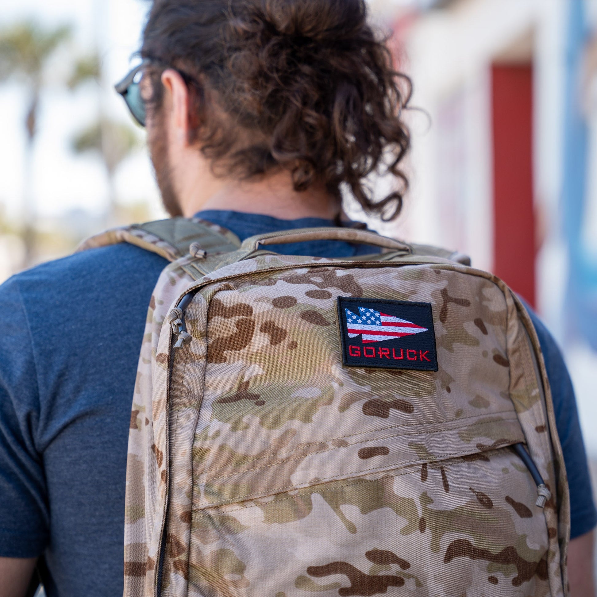 Man in an urban environment carrying a desert camouflage GoRuck rucksack