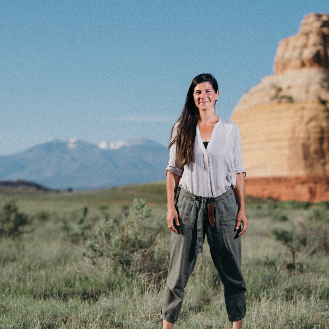 Woman standing in a field with mountains and a red rock formation in the background