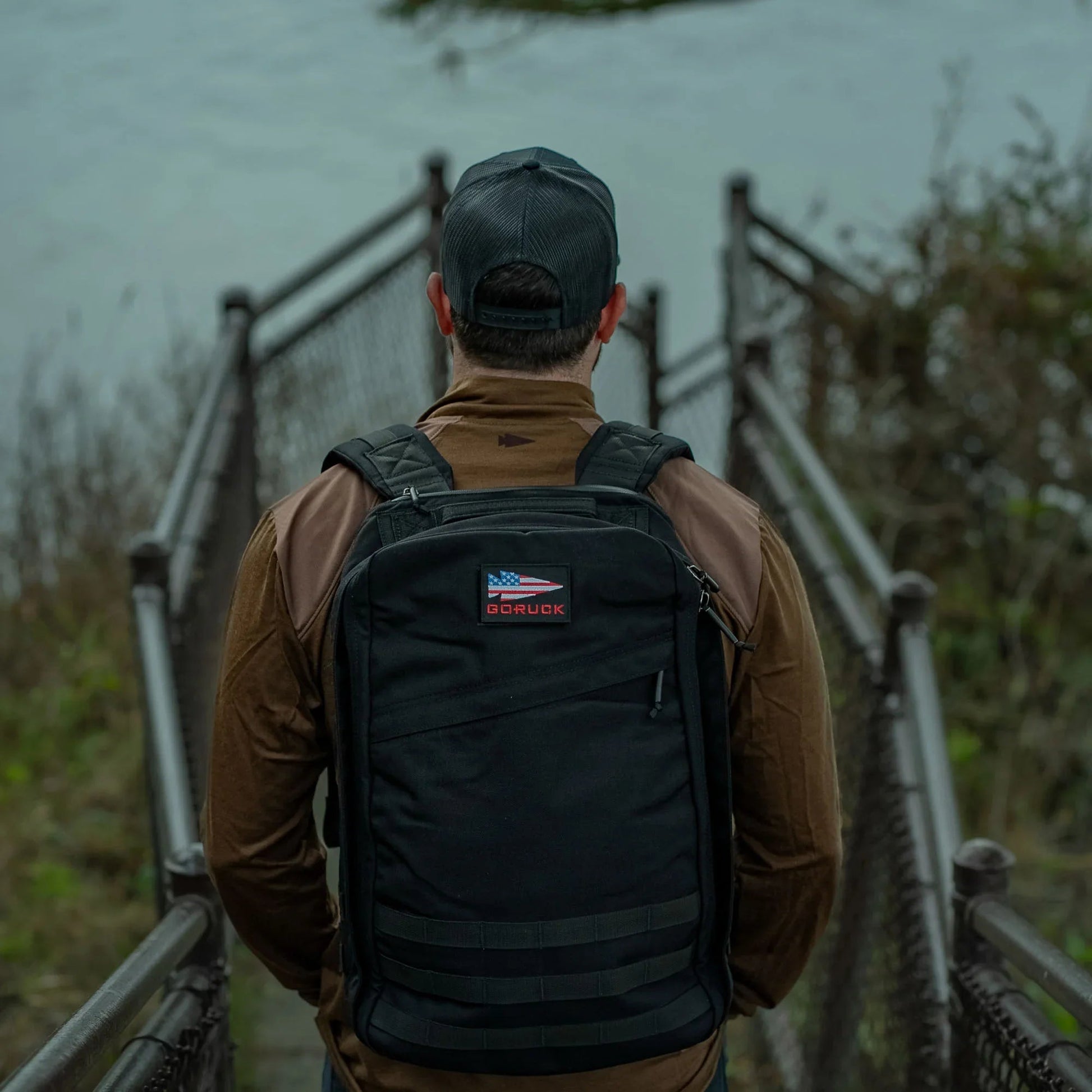 Man wearing black GoRuck rucksack walking down a pathway to the water