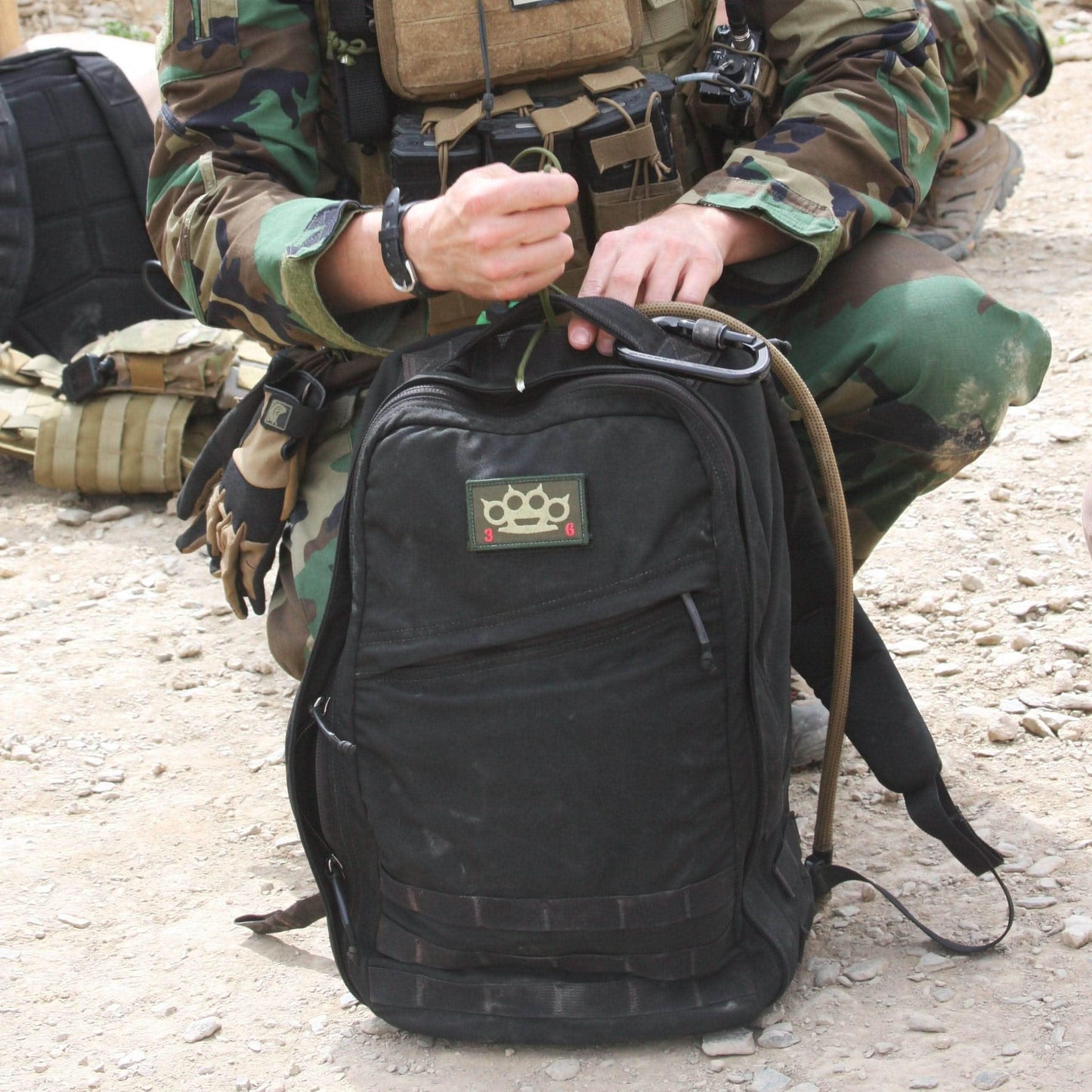 Soldier wearing camouflage kneeling over a black GoRuck rucksack