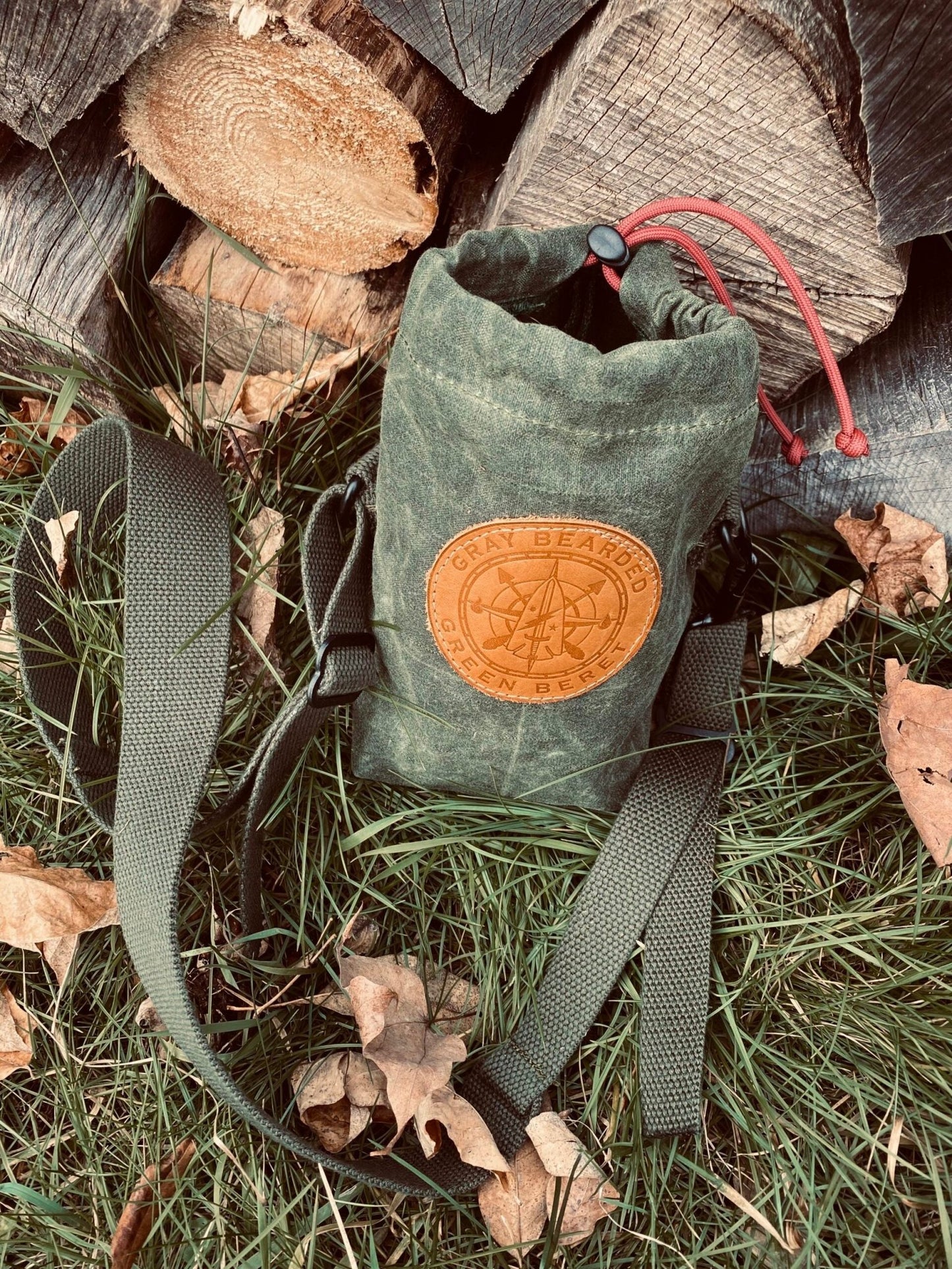 GB2 Waxed Canvas Water Bottle Carrier with Adjustable Strap next to woodpile 