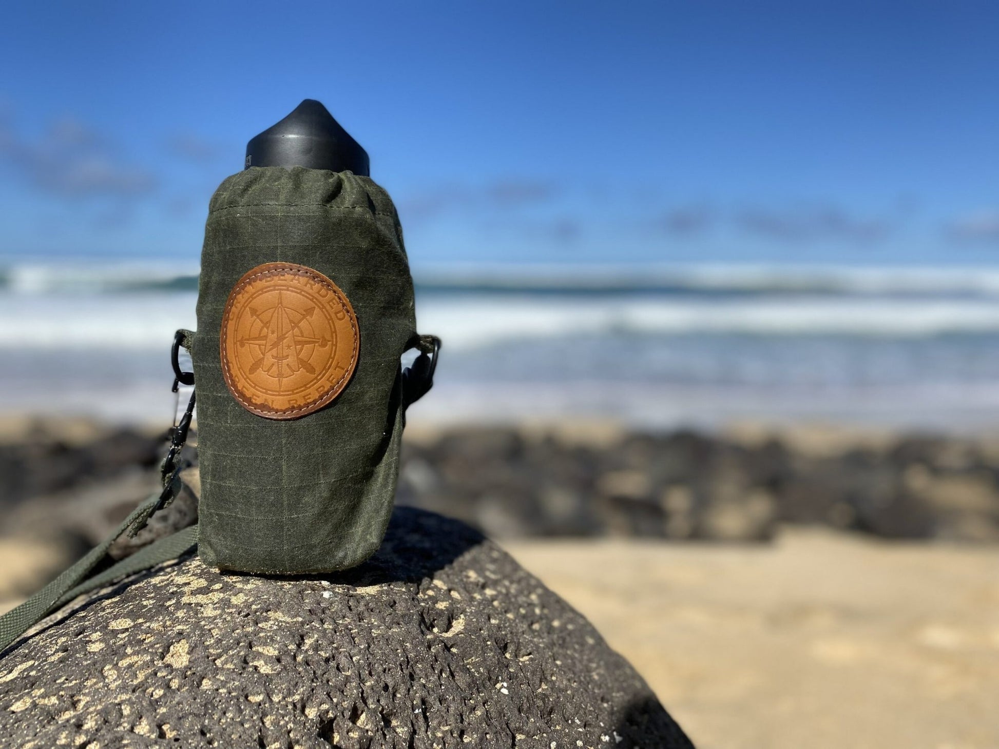 Waxed Canvas Water Bottle Carrier with Adjustable Strap on rock with water bottle inside at beach